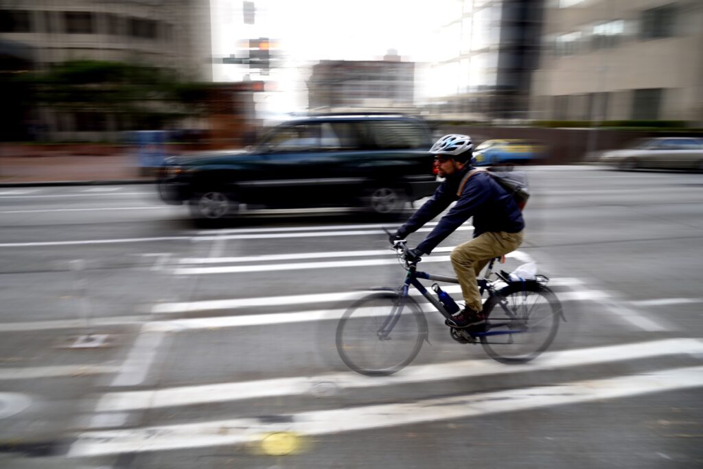 A cyclist wearing a helmet rides legally through a city intersection, representing road safety and vehicle rights under Florida law.